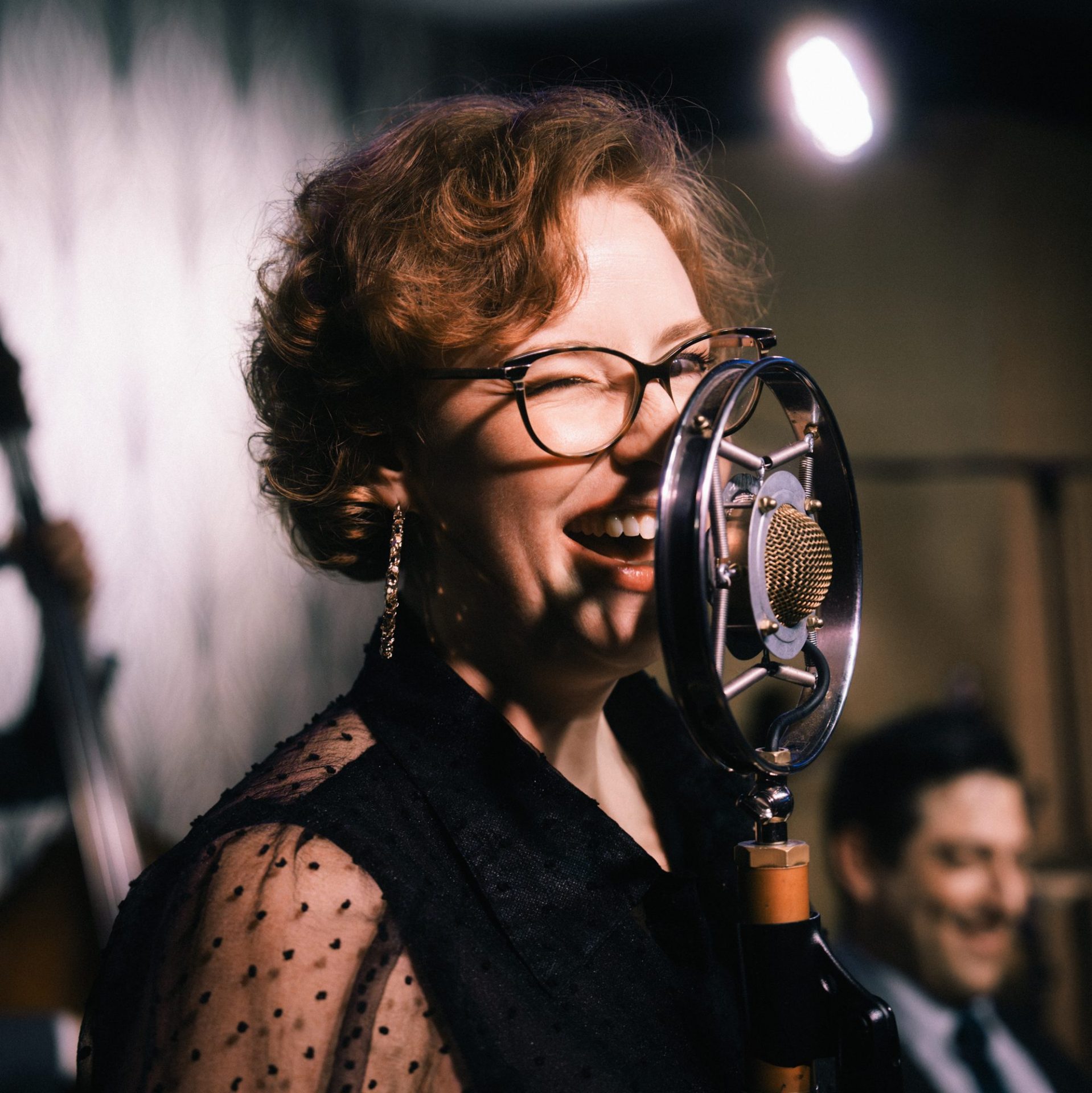 Cantante con gafas interpreta una canción frente a un micrófono de estilo vintage.