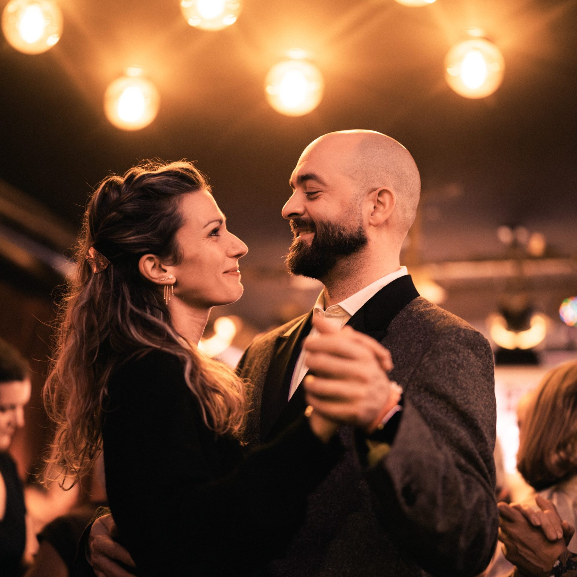 Pareja sonriente bailando bajo luces cálidas durante una fiesta.