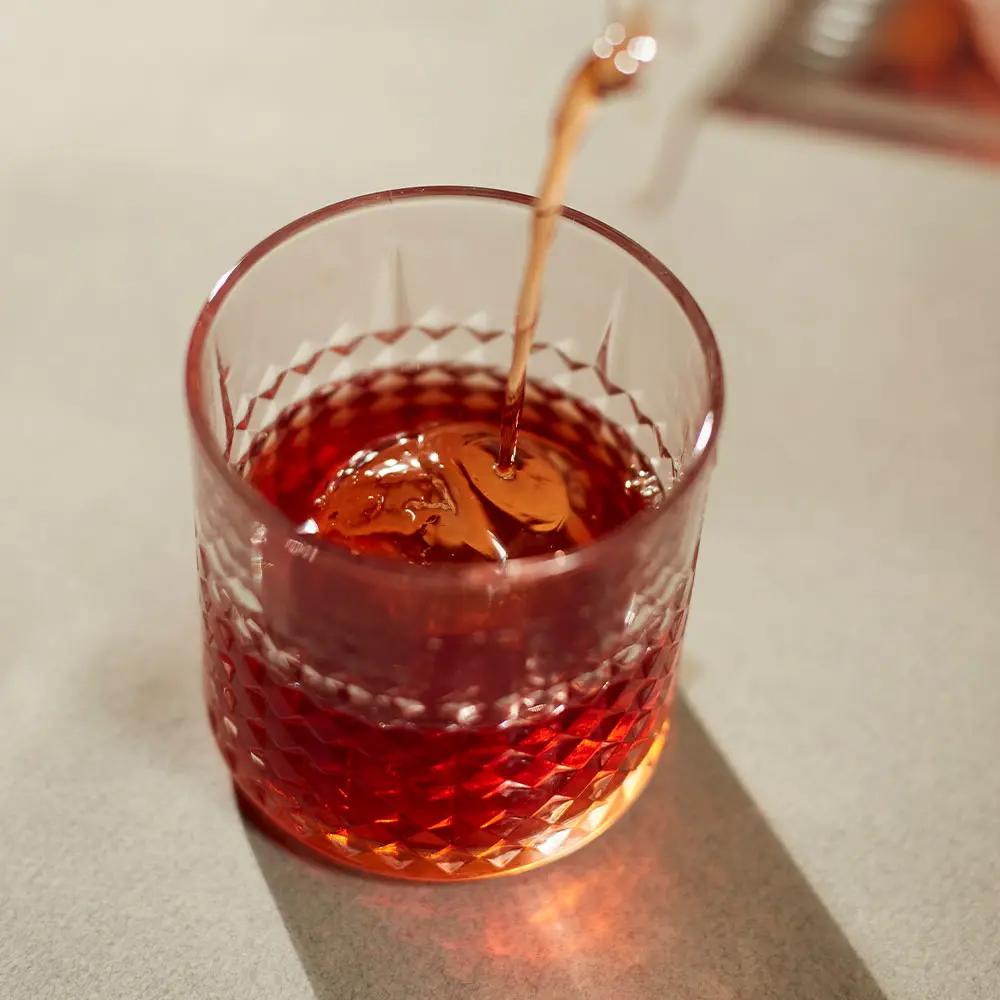 Bebida roja servida sobre hielo en un vaso bajo de cristal tallado.